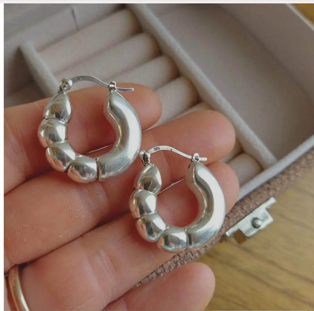 Primer plano de una oreja con un pendiente de aro de plata con cuentas.