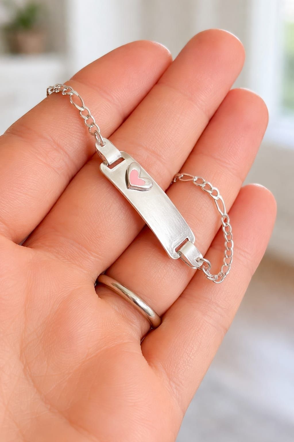 Mano que lleva una pulsera plateada con un dije de corazón rosa sobre una manga rosa suave.