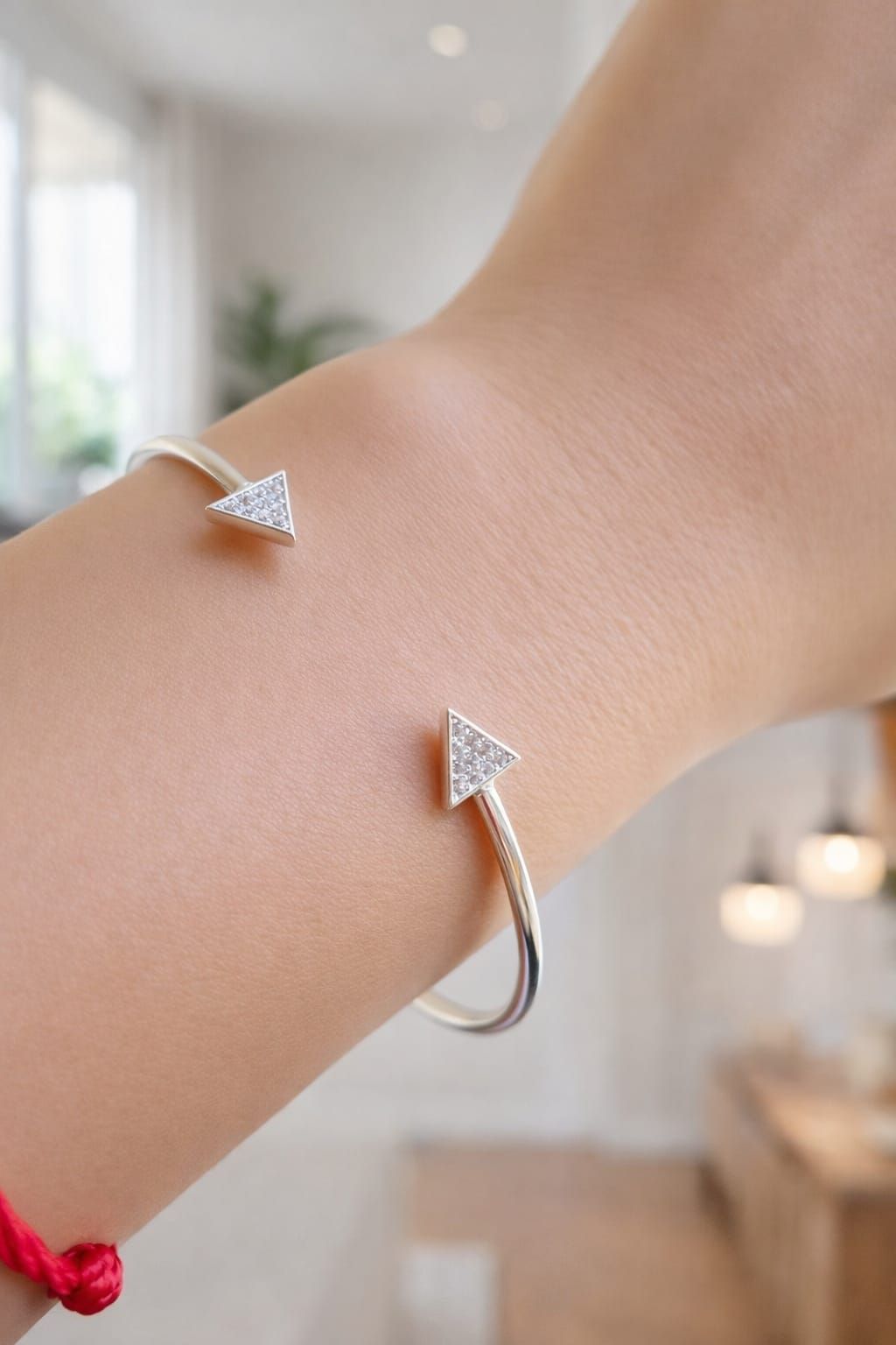 Mano sosteniendo una pulsera plateada ajustable de puño abierto con dos extremos en forma de flecha sobre un fondo blanco.