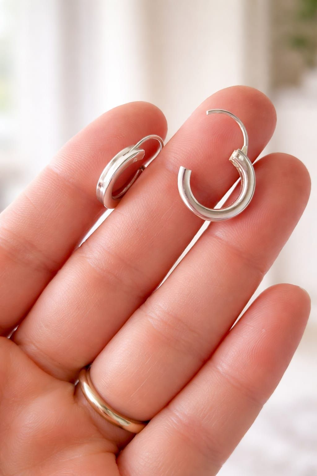 Mano sosteniendo dos anillos de plata sobre un fondo interior suavemente desenfocado.