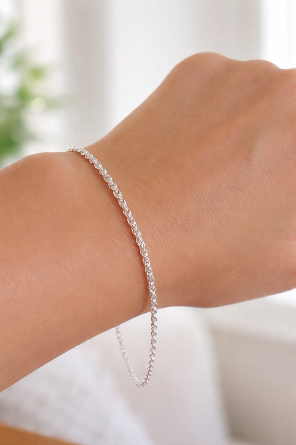 Pulsera de cadena plateada en una muñeca sobre un fondo suave y desenfocado.
