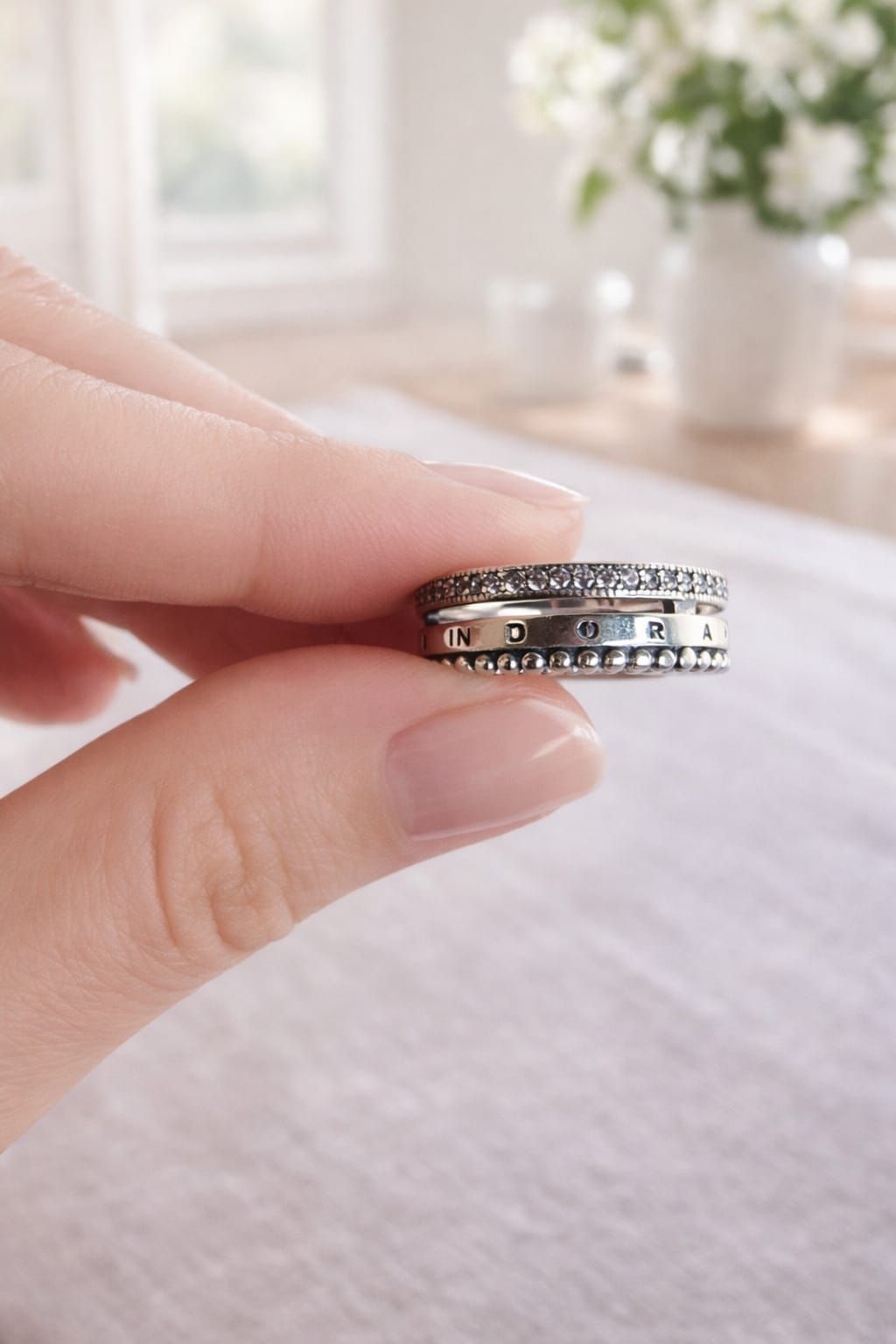 Una mano con anillos apilados de plata con pequeñas piedras descansa sobre un sofá beige.