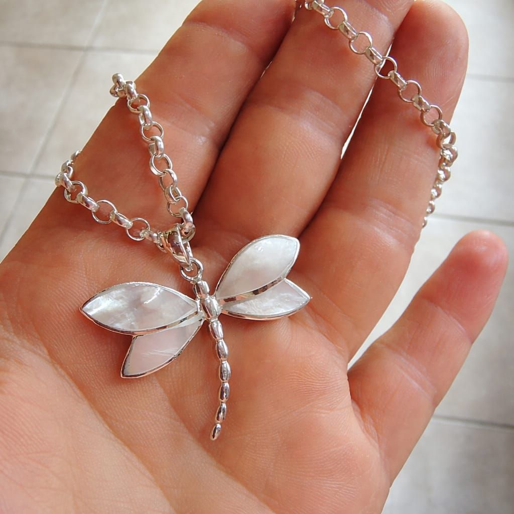 Collar con colgante de libélula plateada en el cuello de una persona, con alas de piedras preciosas blancas y transparentes.