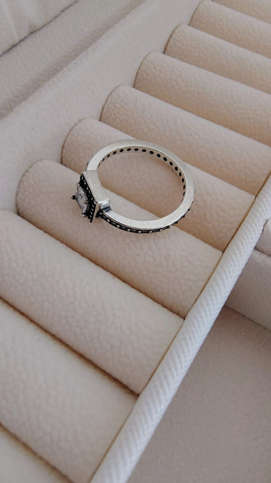 Primer plano de una mano que luce un anillo cuadrado de diamantes con una banda plateada y detalles oscuros.