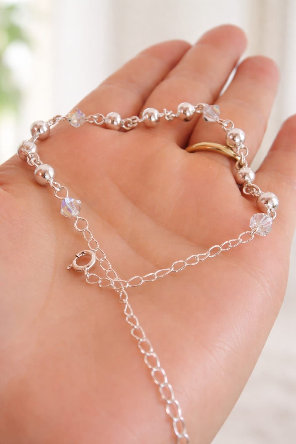 Pulsera de cristal en una muñeca, con piedras transparentes y moradas en una habitación luminosa.