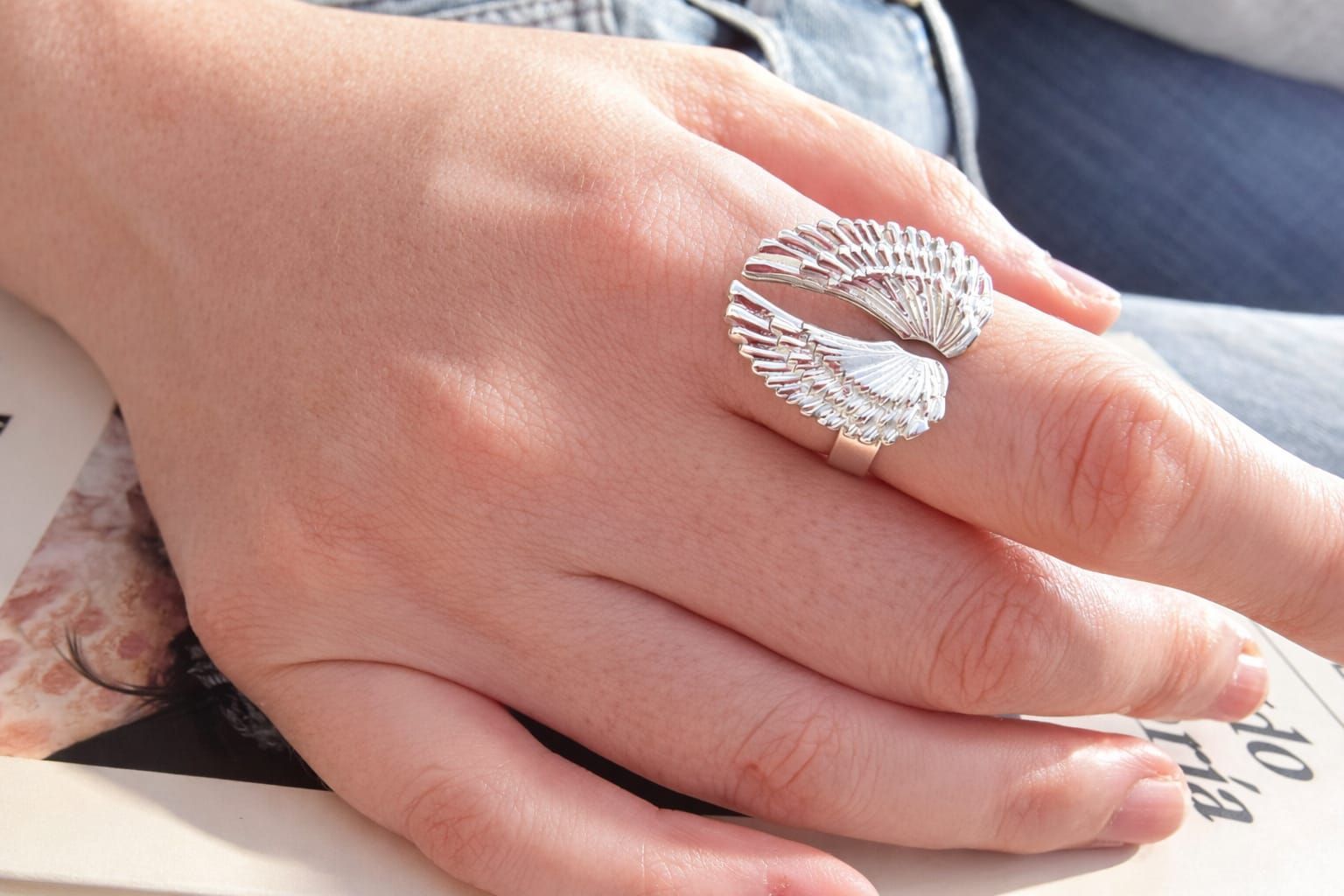 Una mano con un anillo de concha de plata descansa sobre un regazo bajo una suave luz del día.