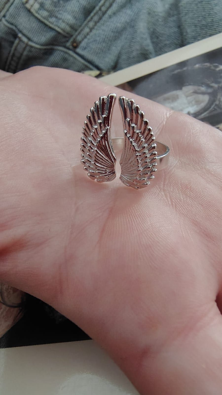 Una mano con un anillo de concha de plata descansa sobre un regazo bajo una suave luz del día.