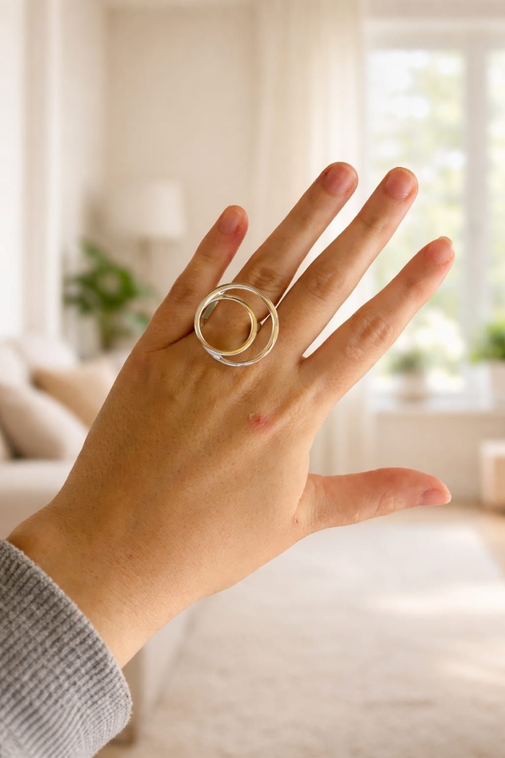 Mano con anillos de plata alzada en una sala de estar tenuemente iluminada.