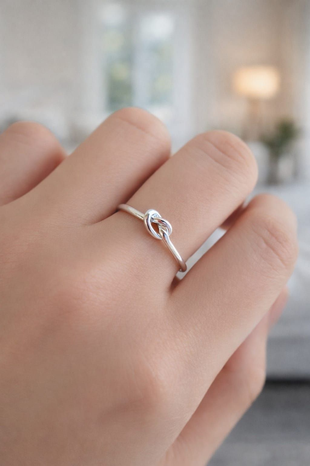 Primer plano de una mano que luce un delicado anillo de plata con una piedra transparente.