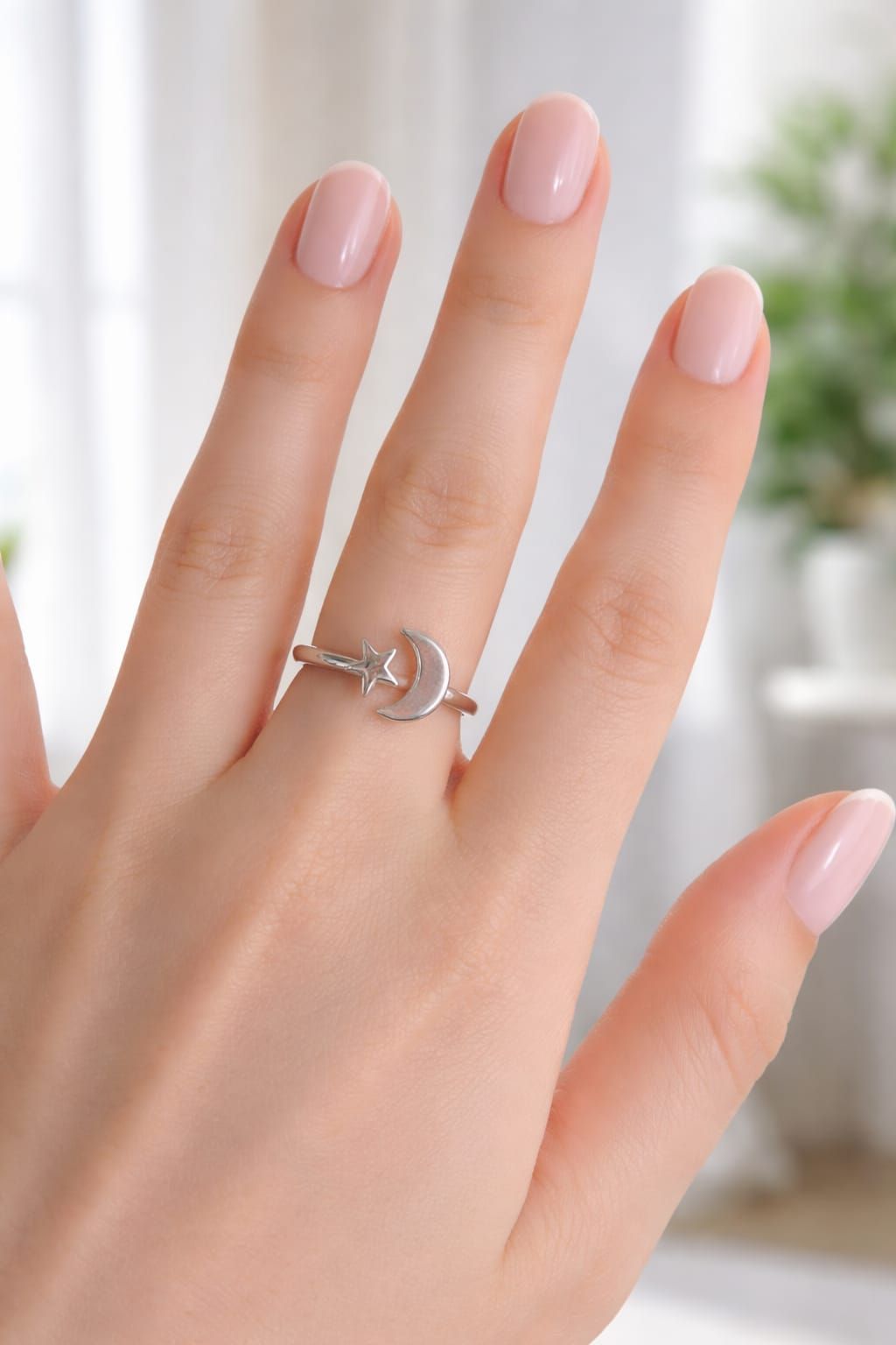Mano sosteniendo un anillo de plata con forma de luna creciente y estrella bajo una suave luz natural.