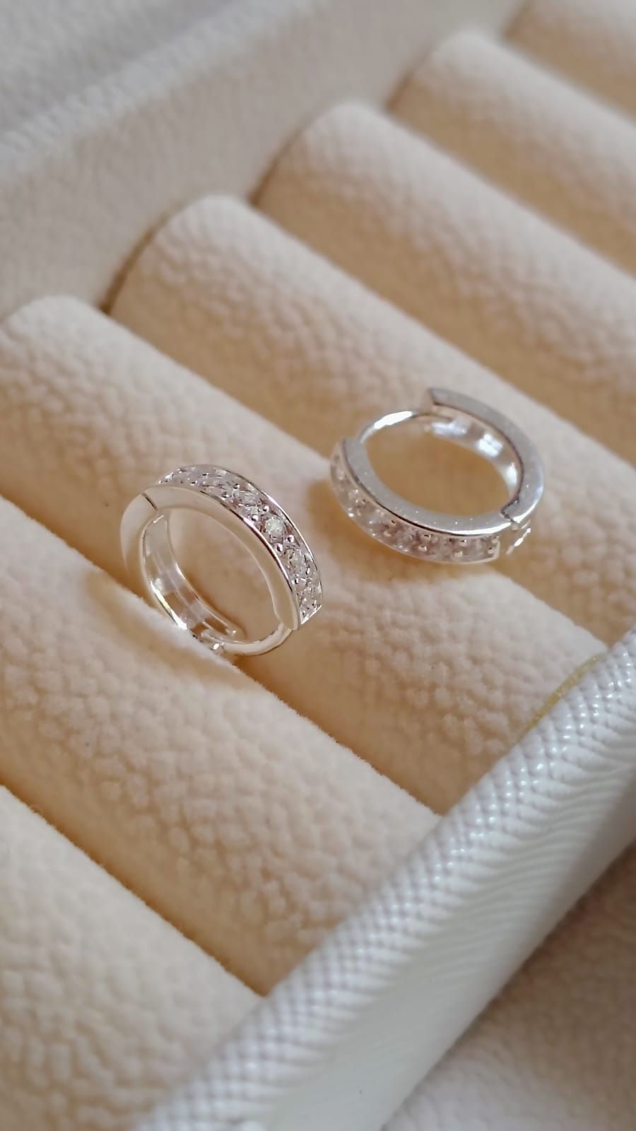 Una mano sostiene dos anillos de plata con piedras transparentes en una sala de estar con iluminación tenue.