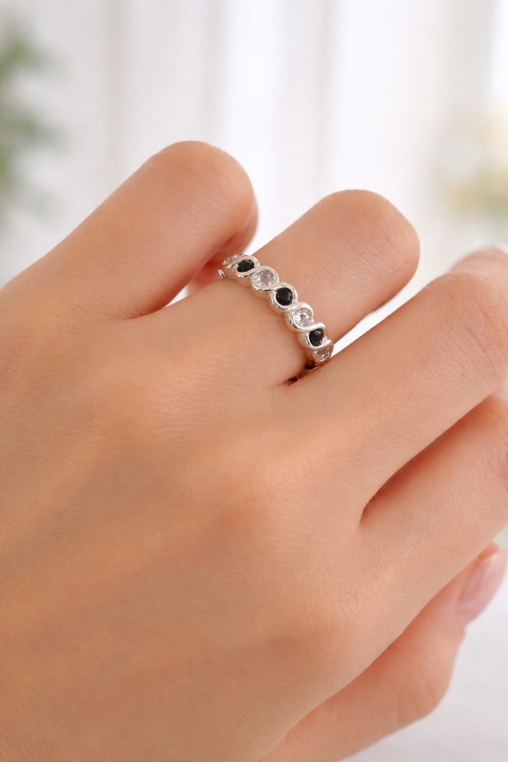Mano sosteniendo un anillo de plata con piedras preciosas negras sobre un fondo suave y desenfocado.