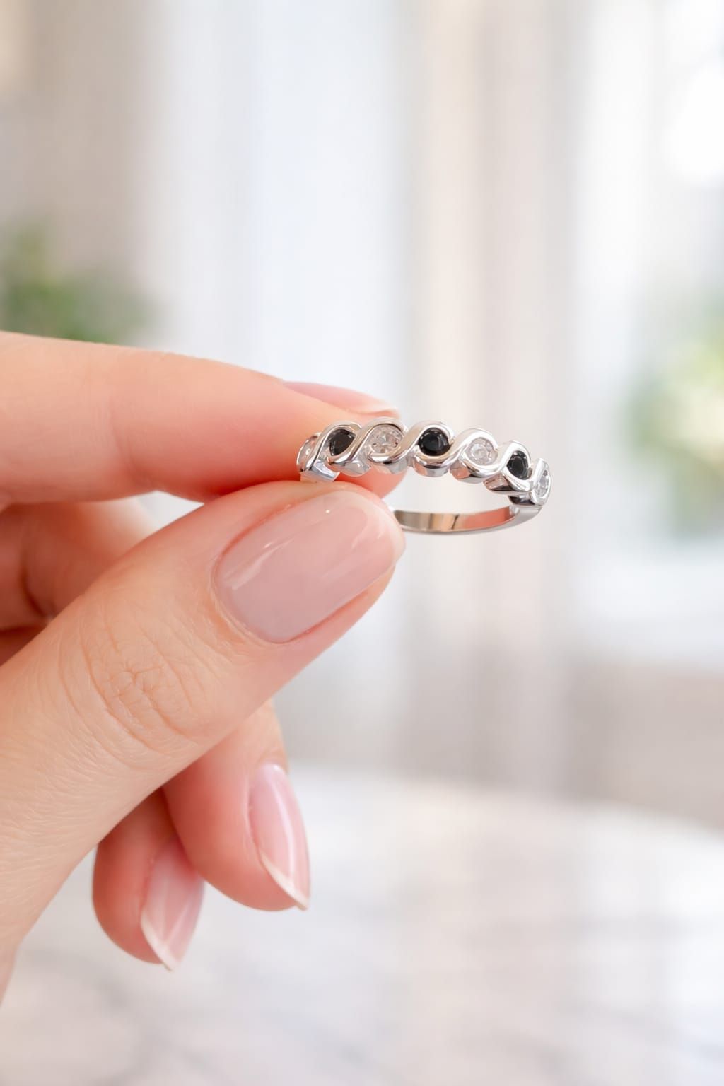 Mano sosteniendo un anillo de plata con piedras preciosas negras sobre un fondo suave y desenfocado.