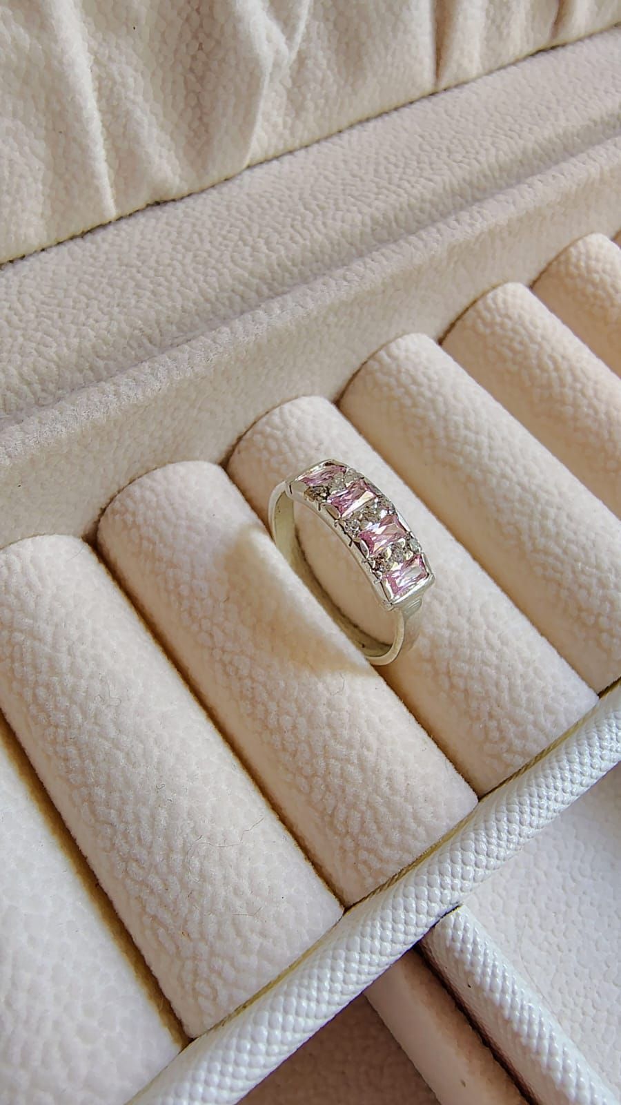 Anillo de oro con piedras rosas en un joyero color crema.