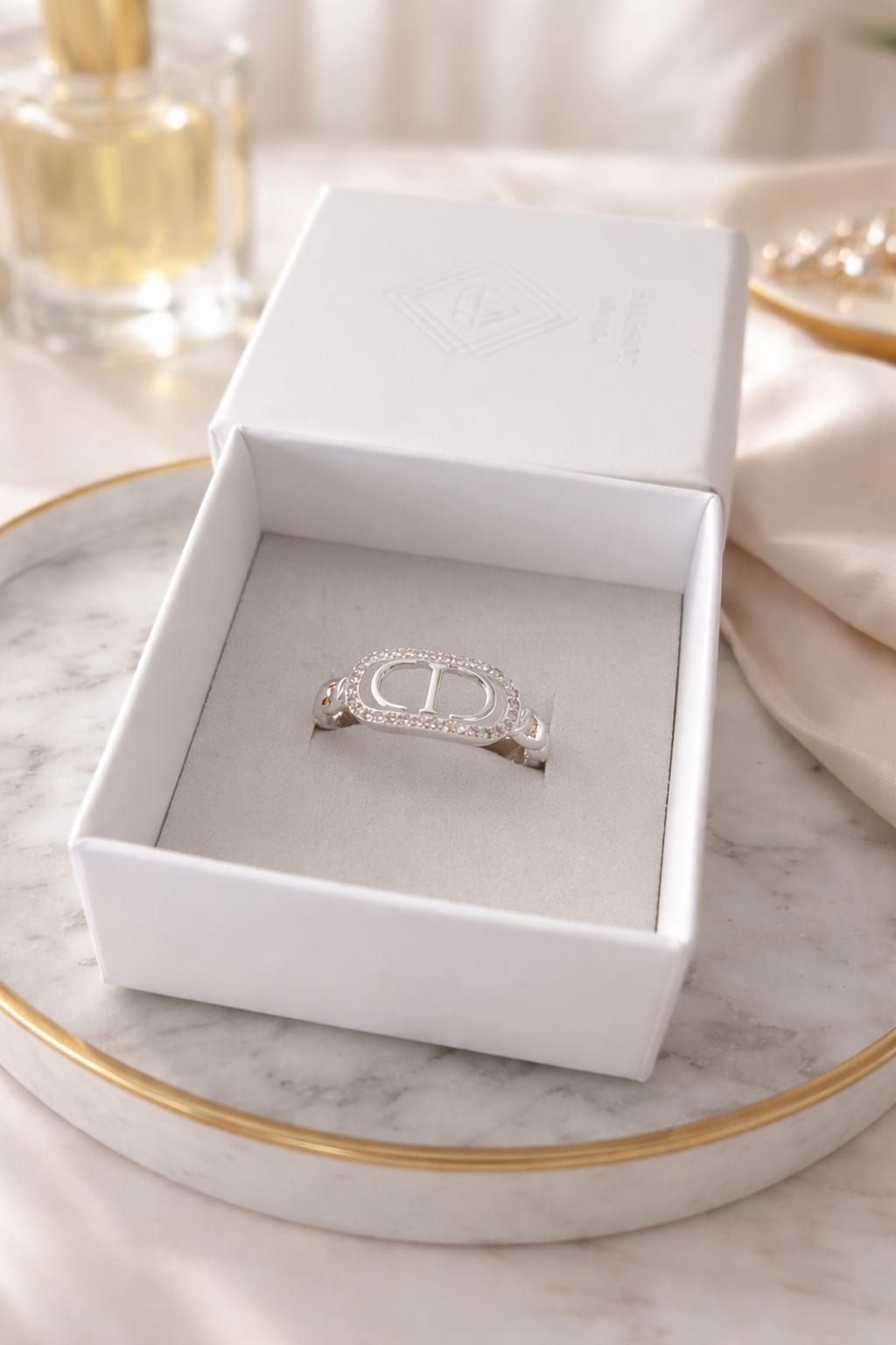 Un anillo de diamantes en un joyero blanco sobre una mesa con decoración en tonos beige suaves.