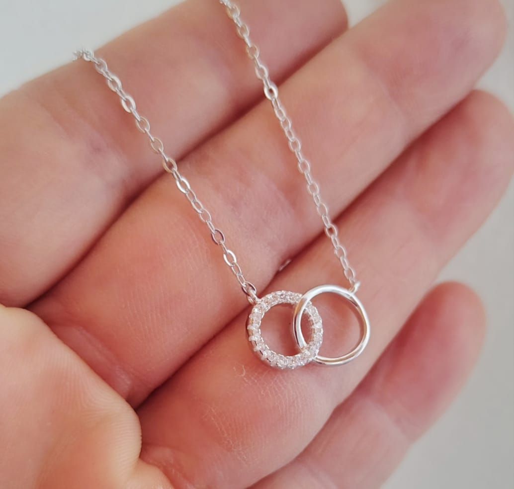 Primer plano de una persona sonriente que lleva un collar de plata con anillos entrelazados.