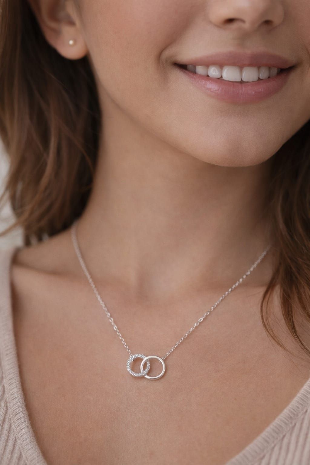 Primer plano de una persona sonriente que lleva un collar de plata con anillos entrelazados.
