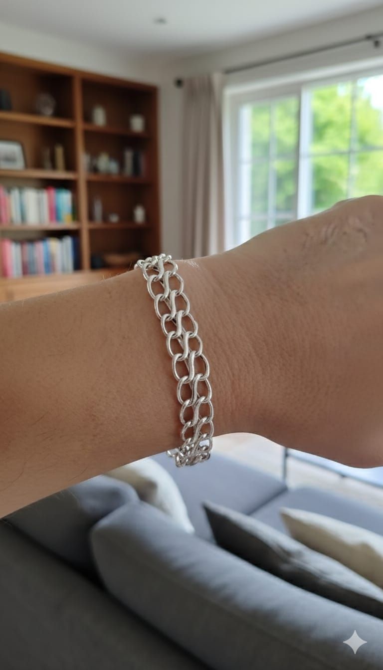 Pulsera de cadena de plata en la muñeca en una luminosa sala de estar, con un sofá, una estantería y una ventana al fondo.