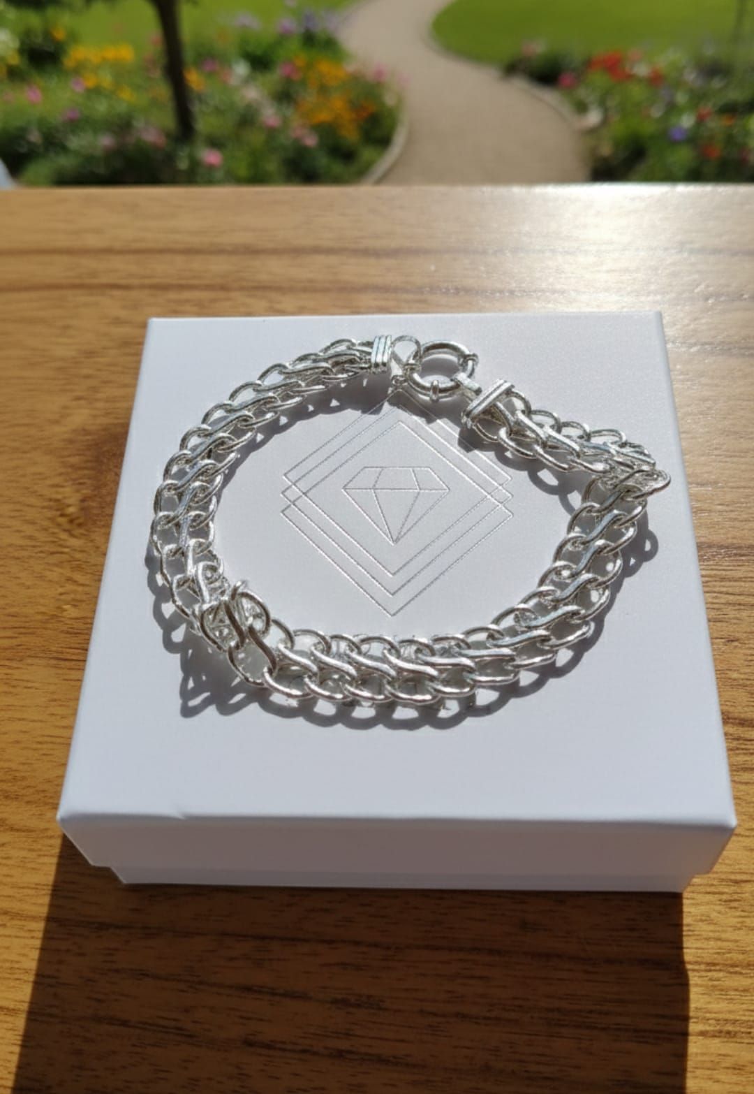Pulsera de cadena de plata en la muñeca en una luminosa sala de estar, con un sofá, una estantería y una ventana al fondo.