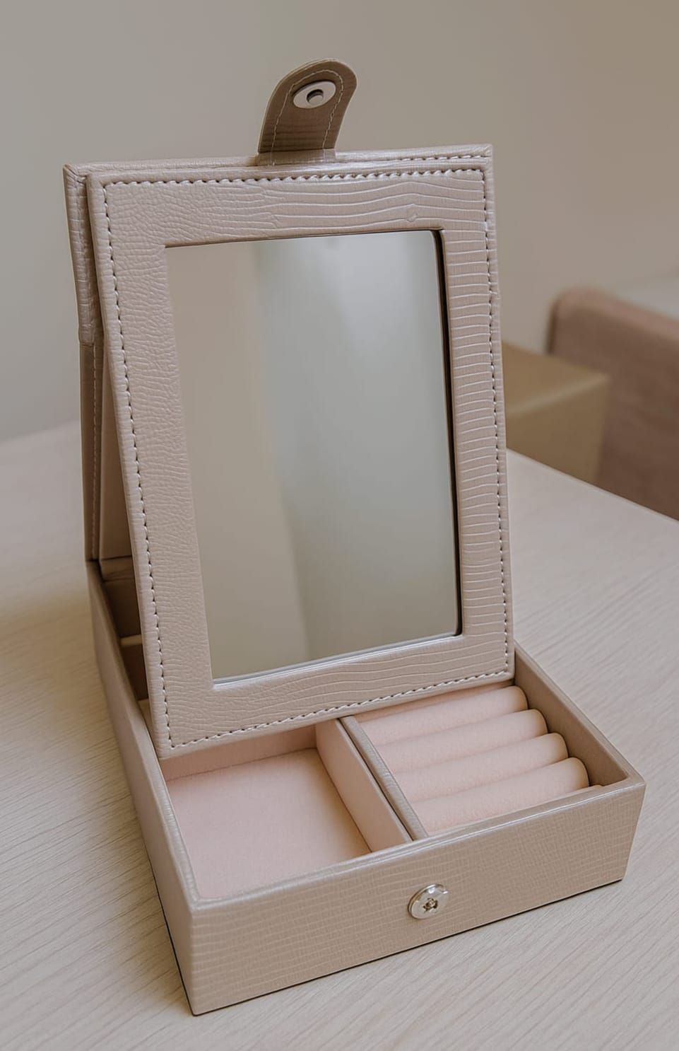 Joyero rosa con espejo, compartimentos abiertos y un espejo de pie sobre una mesa.