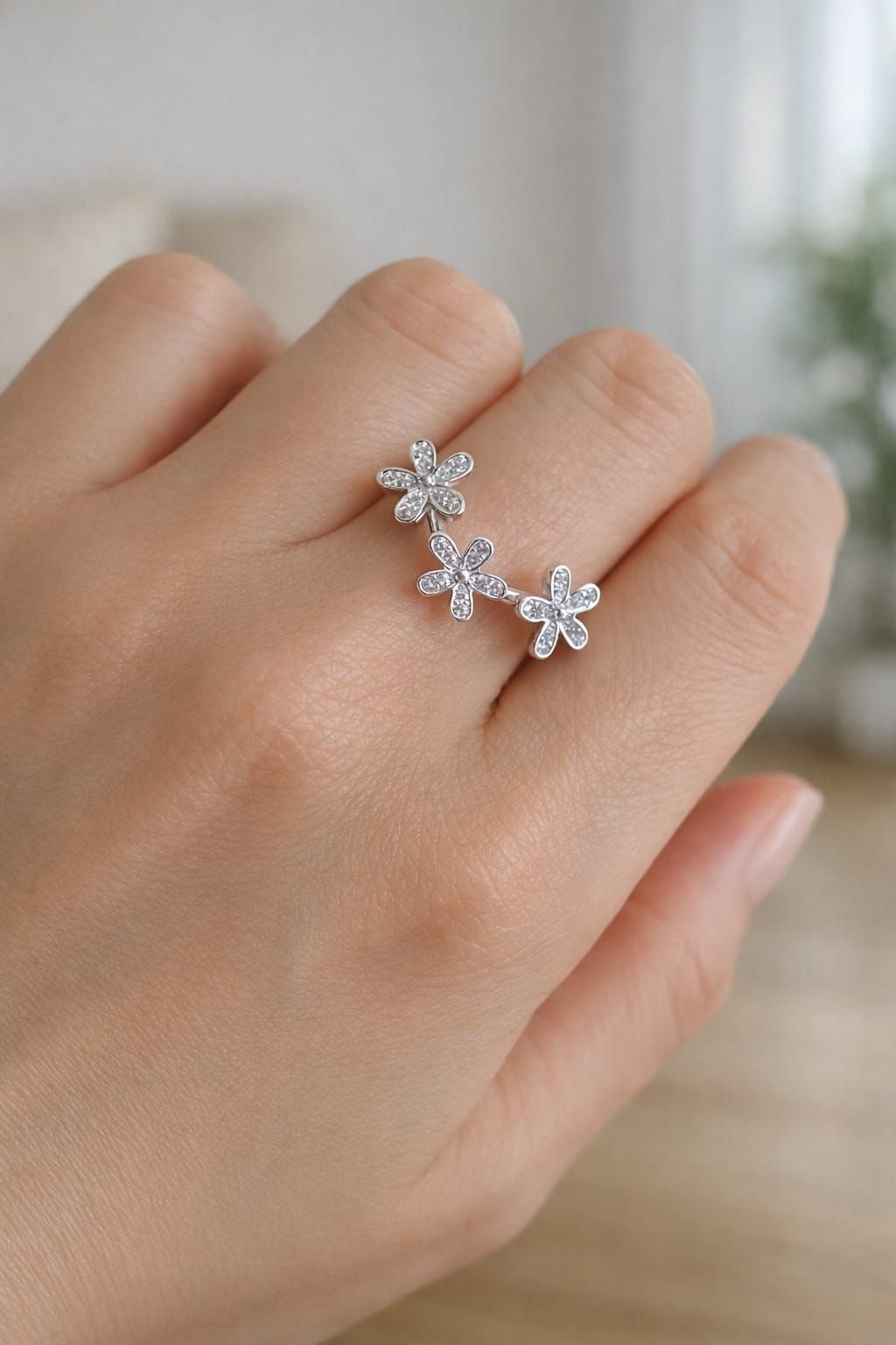 Mano con un delicado anillo de plata en forma de copo de nieve sobre un fondo interior borroso.