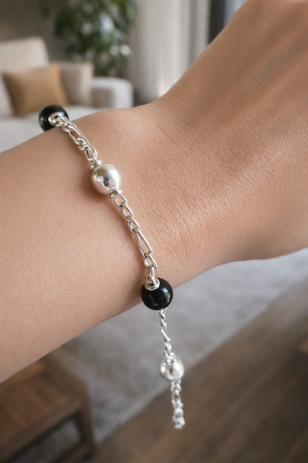 Primer plano de una muñeca que luce una pulsera de cuentas plateadas con detalles en negro y perlas.