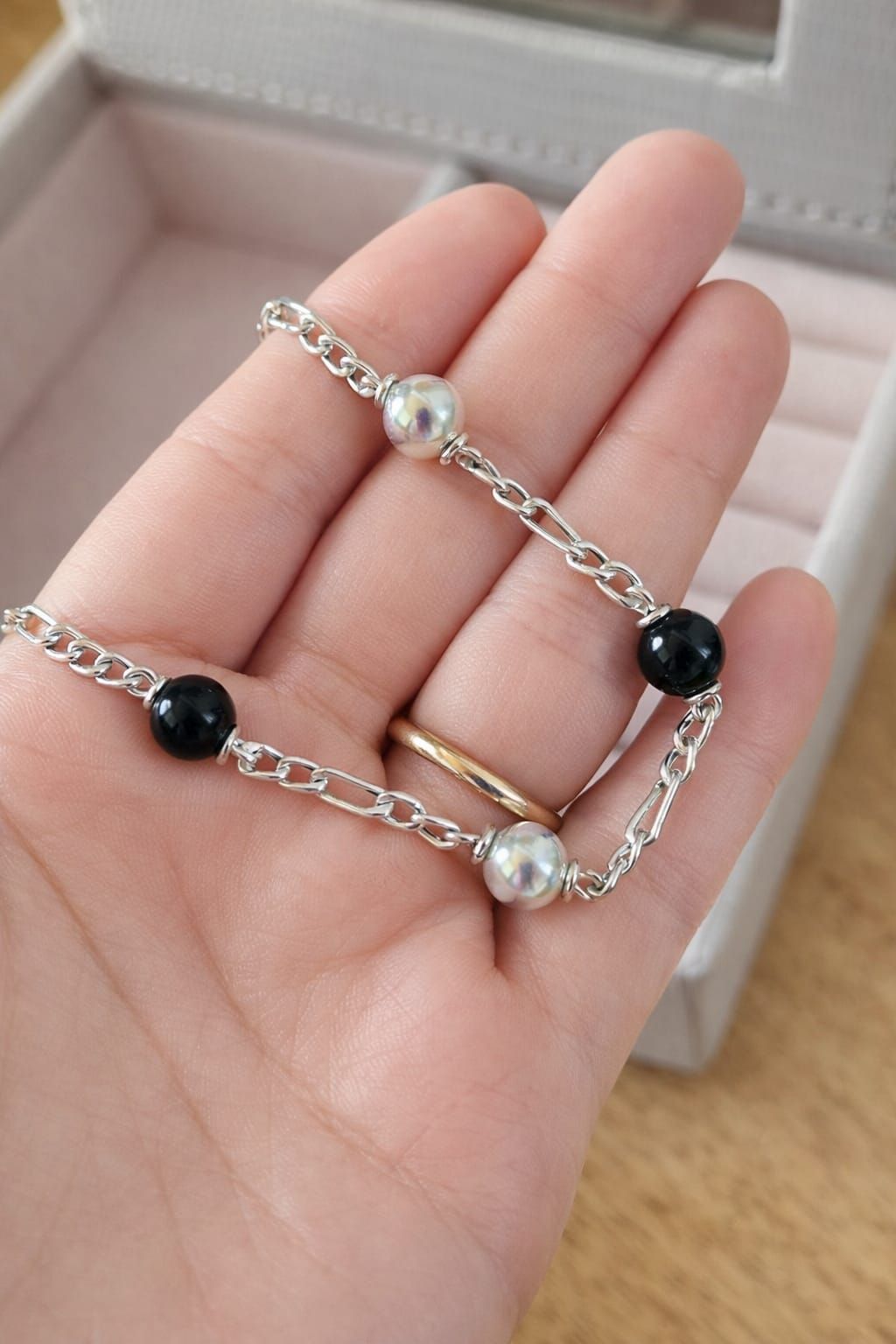 Primer plano de una muñeca que luce una pulsera de cuentas plateadas con detalles en negro y perlas.