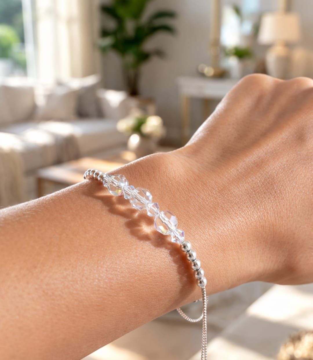 Primer plano de una muñeca que luce una delicada pulsera de plata en un salón luminoso y acogedor.