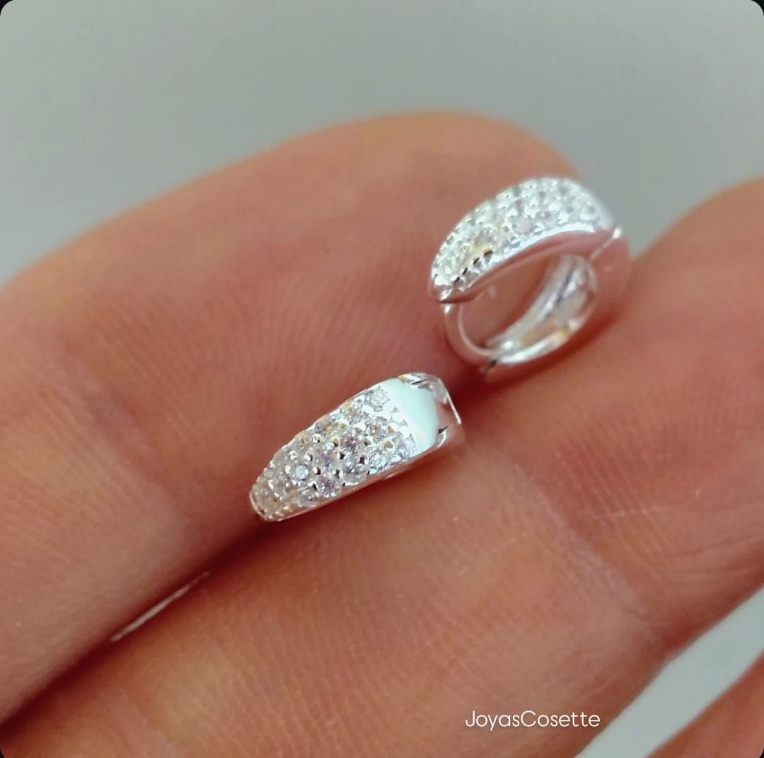 Primer plano de una oreja con un pequeño pendiente colgante de plata sobre un fondo suavemente desenfocado.