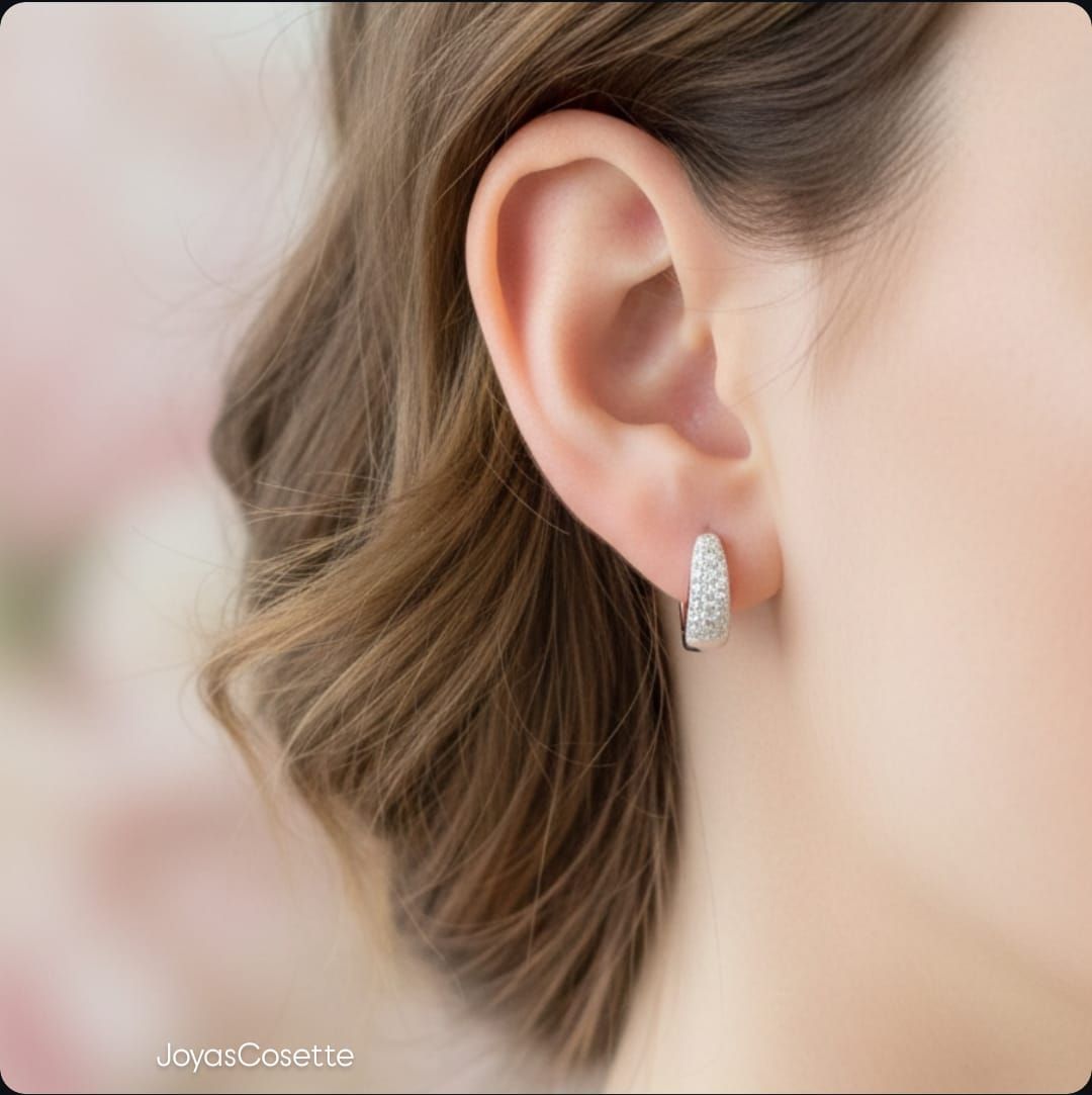 Primer plano de una oreja con un pequeño pendiente colgante de plata sobre un fondo suavemente desenfocado.