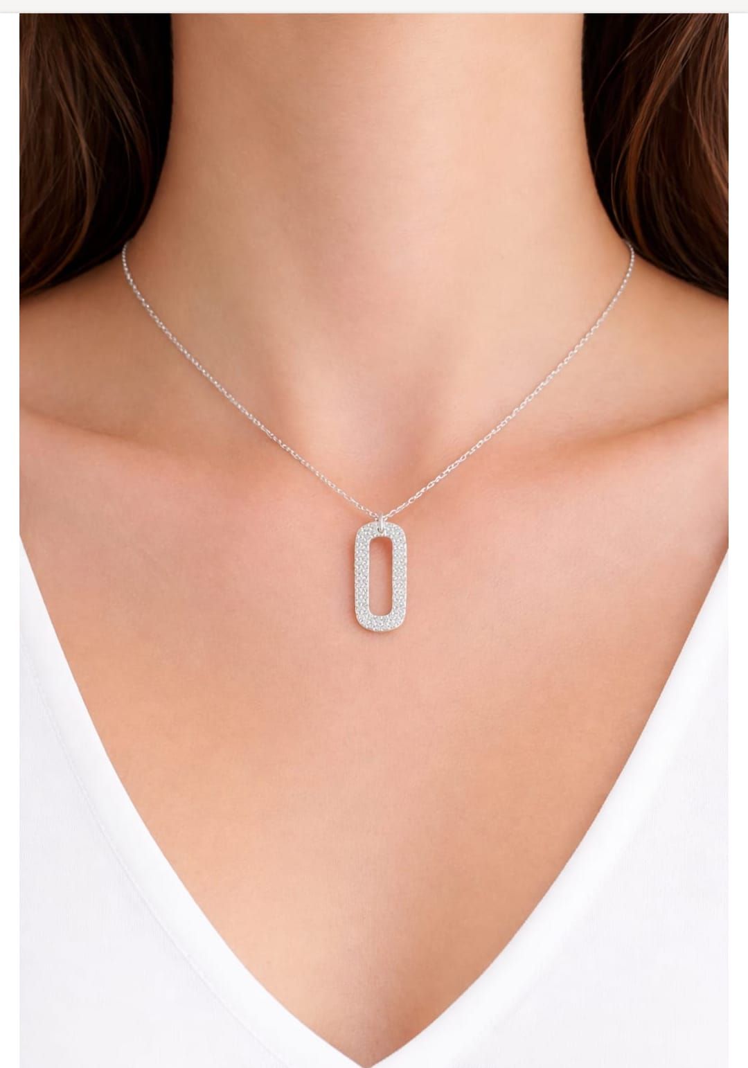 Collar con colgante de plata sobre el cuello, llevado sobre una blusa blanca con escote en V.