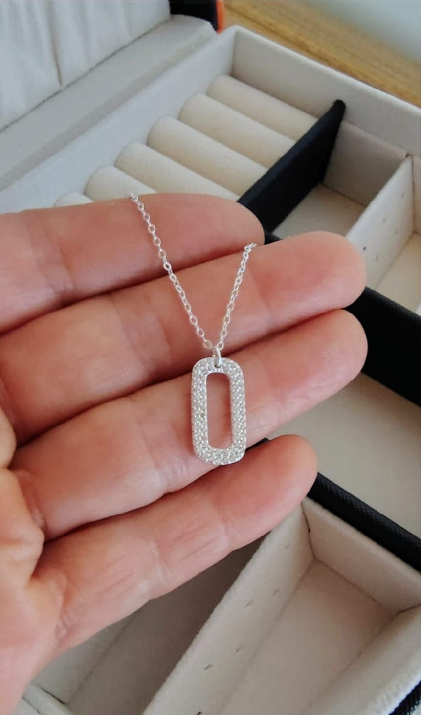 Collar con colgante de plata sobre el cuello, llevado sobre una blusa blanca con escote en V.