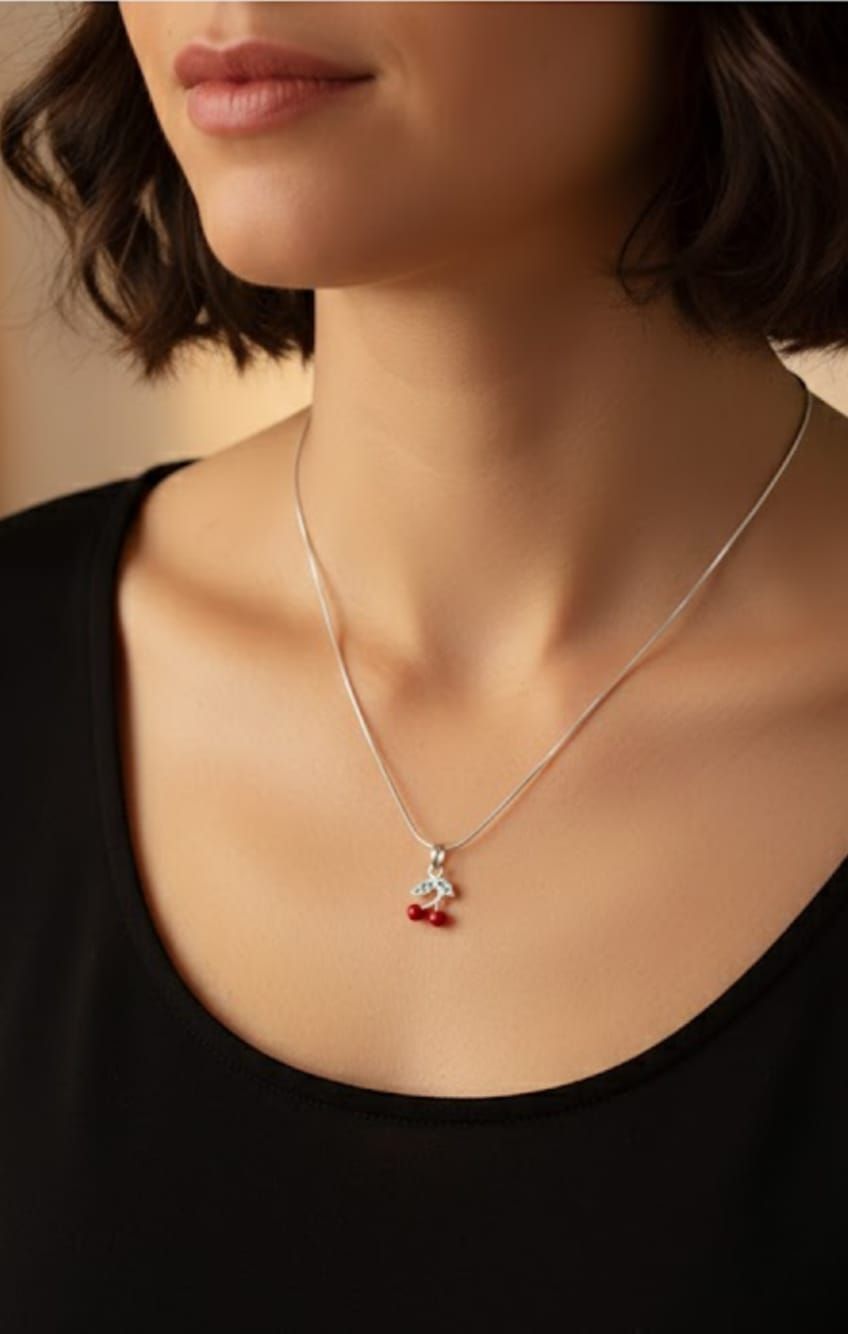 Primer plano de una mujer que lleva un collar plateado con un colgante rojo sobre una blusa negra.