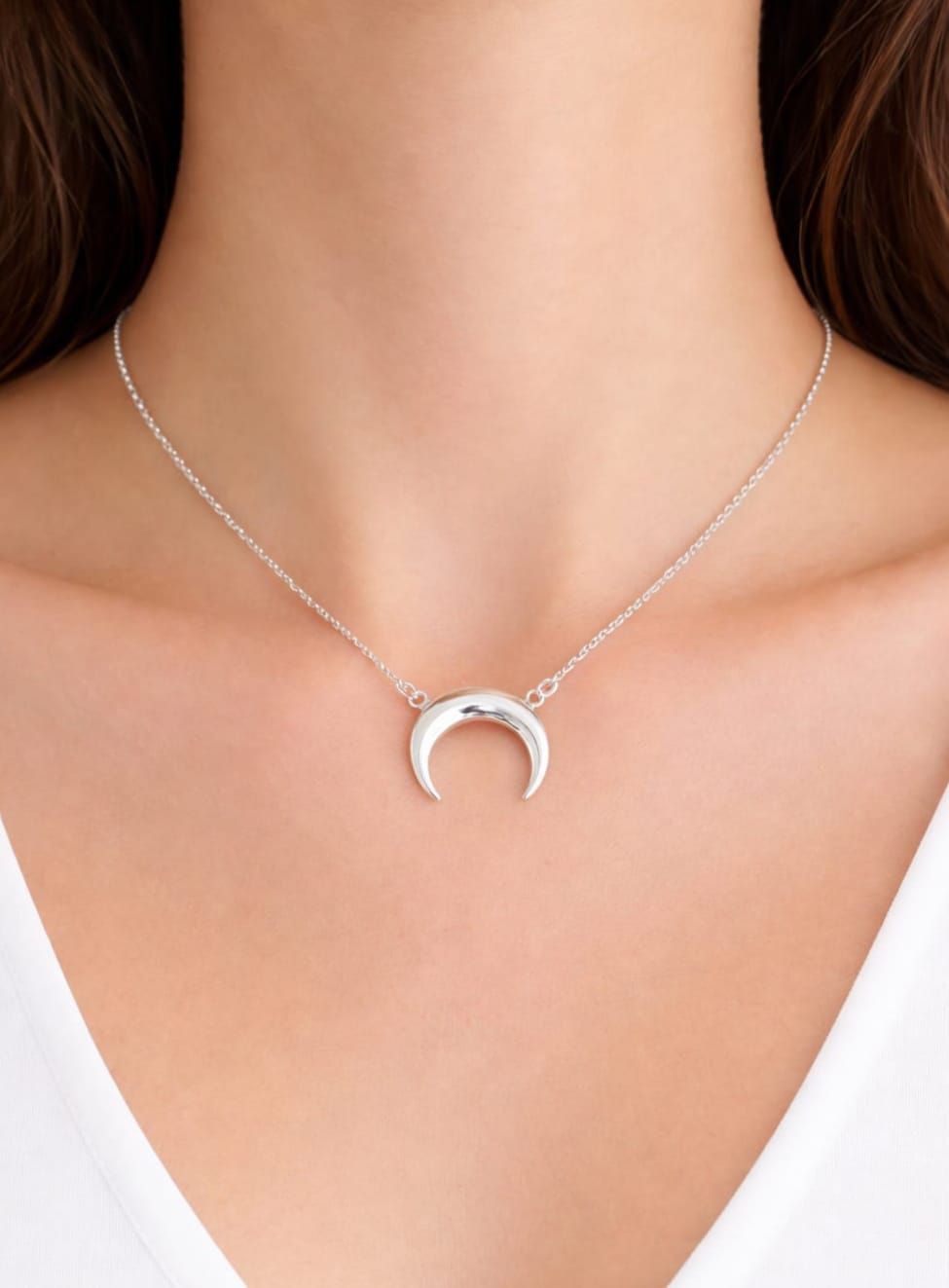 Collar con colgante de luna creciente plateada en el cuello de una mujer, usado con una blusa blanca.
