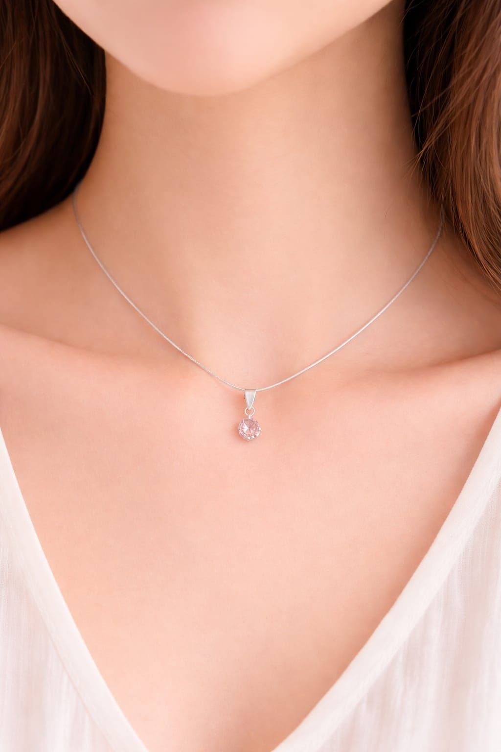 Mano sosteniendo un collar de plata con un pequeño colgante transparente sobre un fondo claro.