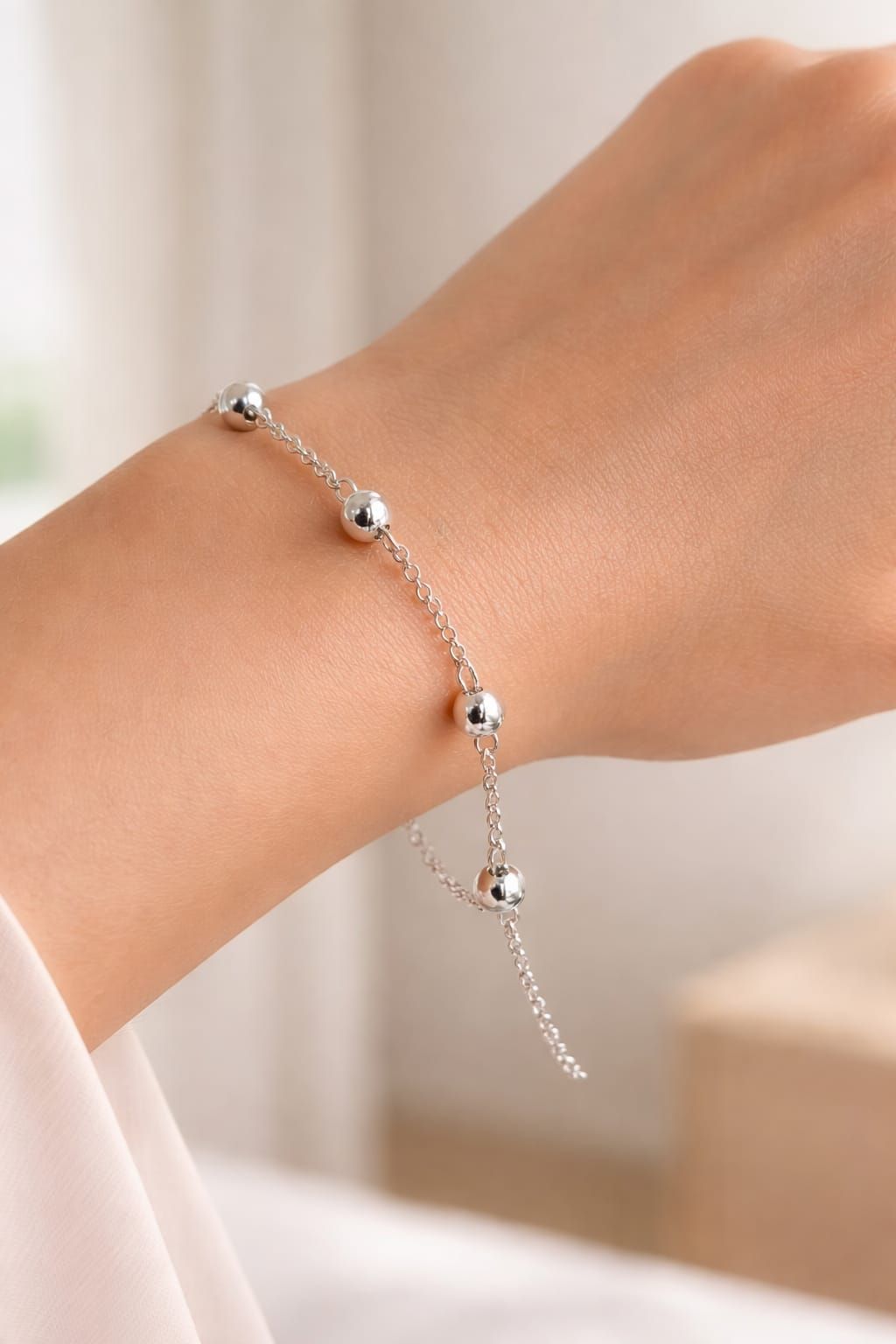 Pulsera de cuentas de plata en la muñeca con un dije colgante y una delicada cadena.