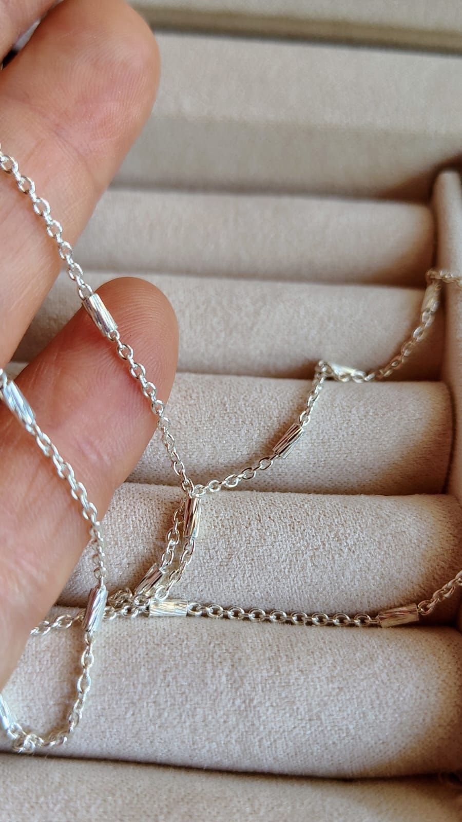 Collar de cadena de plata en el cuello y la parte superior del pecho de una persona sobre un fondo neutro.