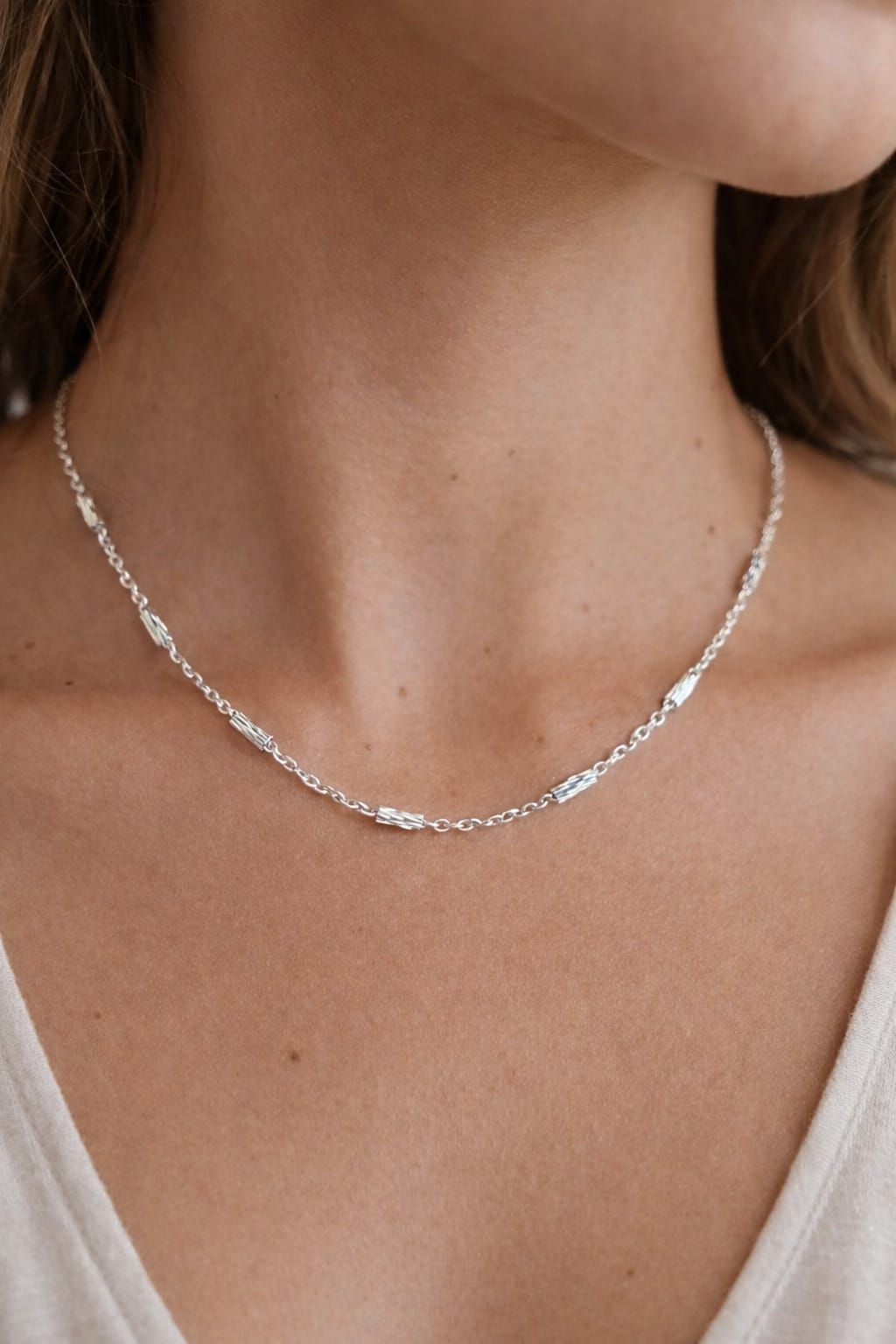 Collar de cadena de plata en el cuello y la parte superior del pecho de una persona sobre un fondo neutro.
