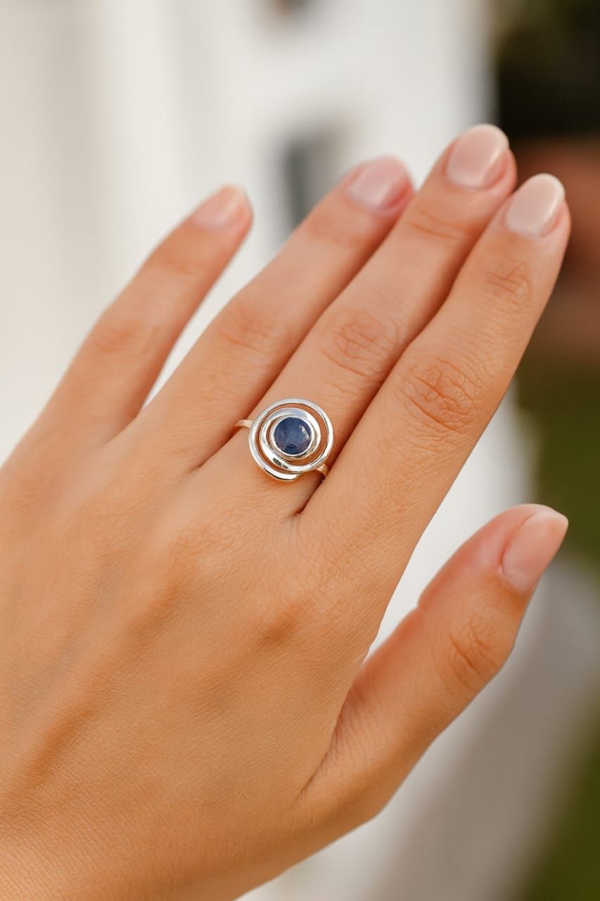 Primer plano de una mano que lleva un anillo de plata con una gema azul y piedras transparentes.