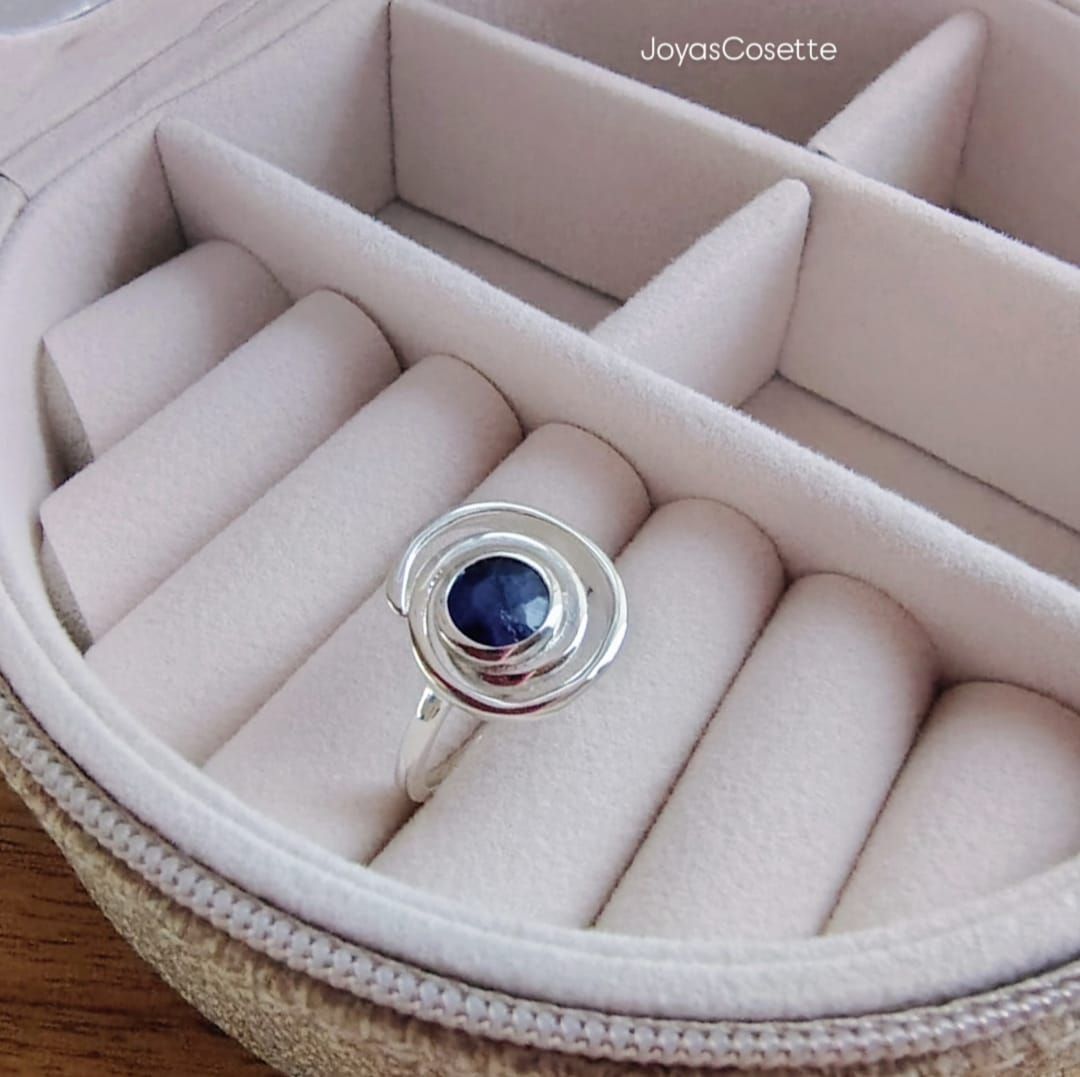 Primer plano de una mano que lleva un anillo de plata con una gema azul y piedras transparentes.