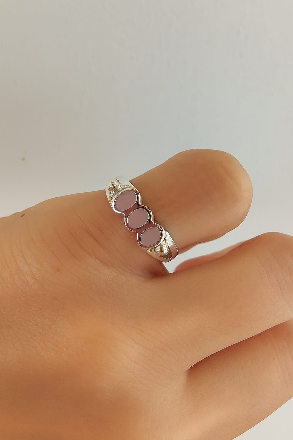 Mano sosteniendo un anillo de plata con pequeñas piedras transparentes sobre un fondo blanco suave.