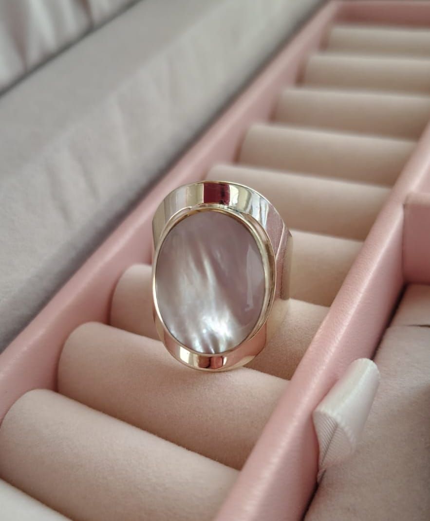 Mano con un gran anillo ovalado de piedra blanca sobre un fondo claro liso.