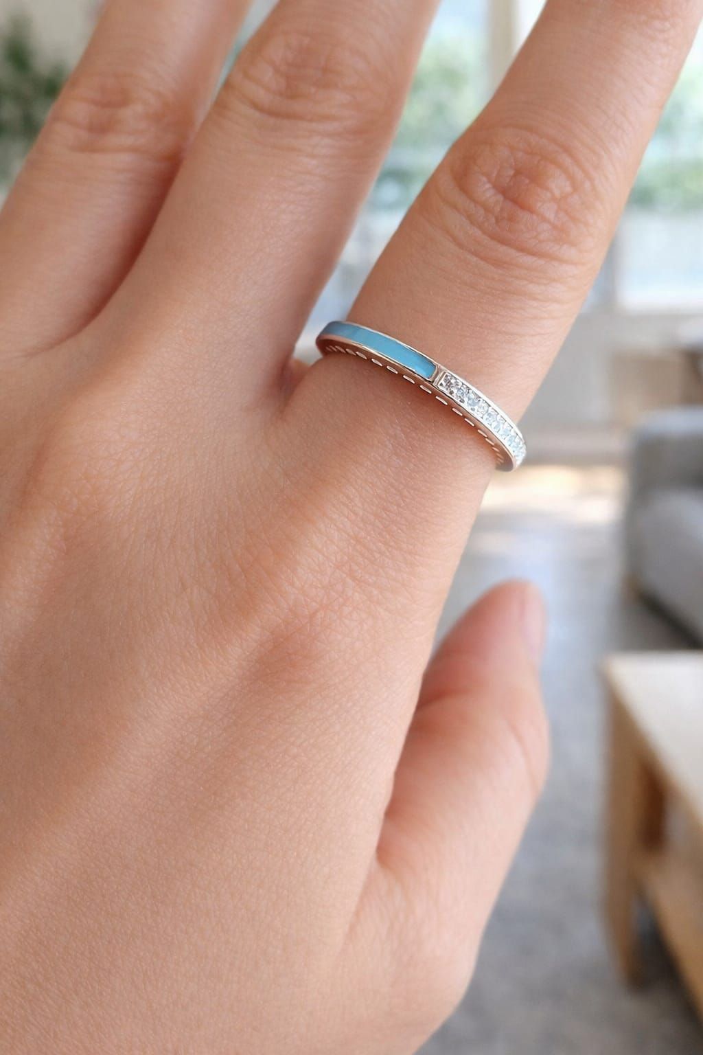 Una mano sostiene un anillo de plata con diamantes incrustados sobre un fondo suavemente iluminado.