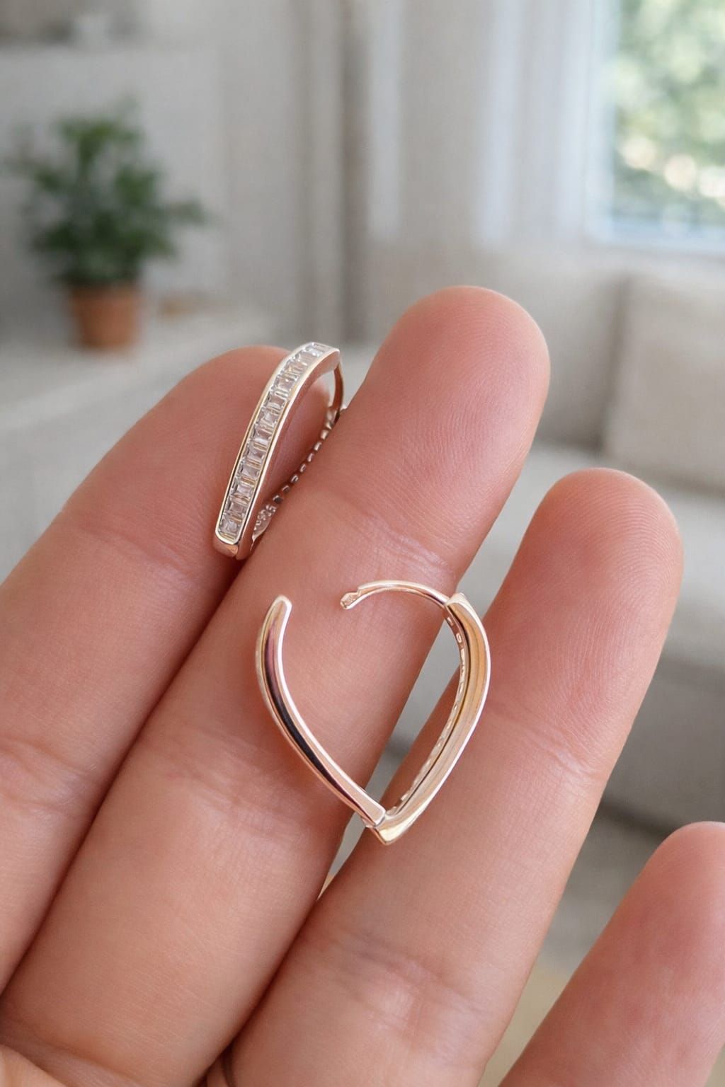 Mano sosteniendo dos delicados anillos de plata, uno en forma de corazón, con un suave fondo interior desenfocado.