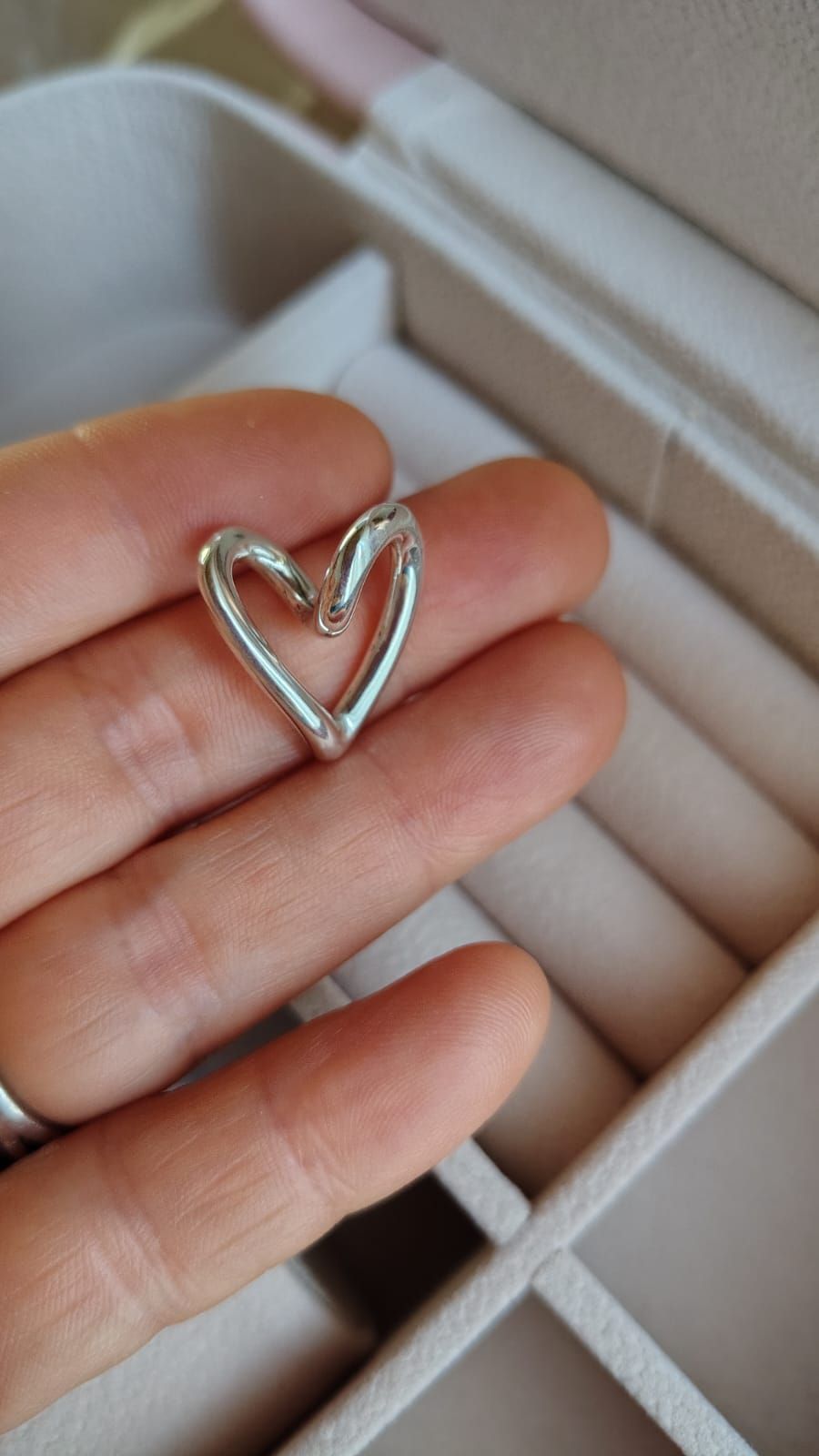 Mano sosteniendo una pulsera de plata con un colgante en forma de corazón y un cierre con incrustaciones de cristal.