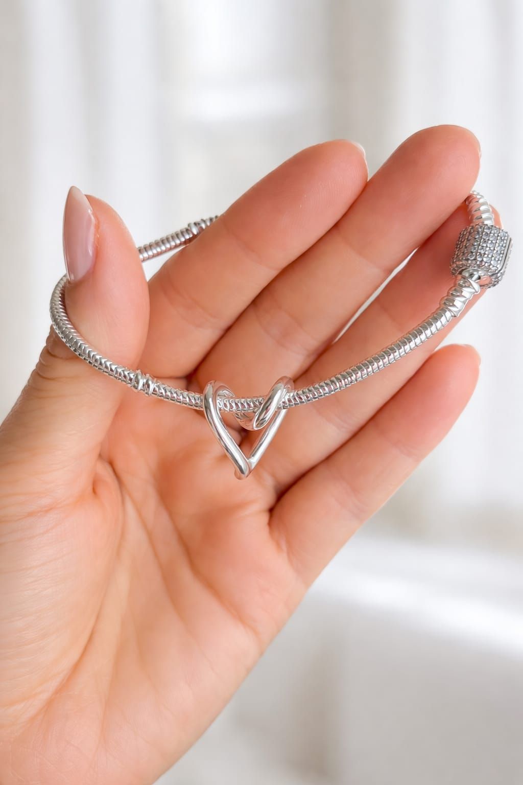 Mano sosteniendo un collar plateado en forma de corazón con un colgante y un broche.
