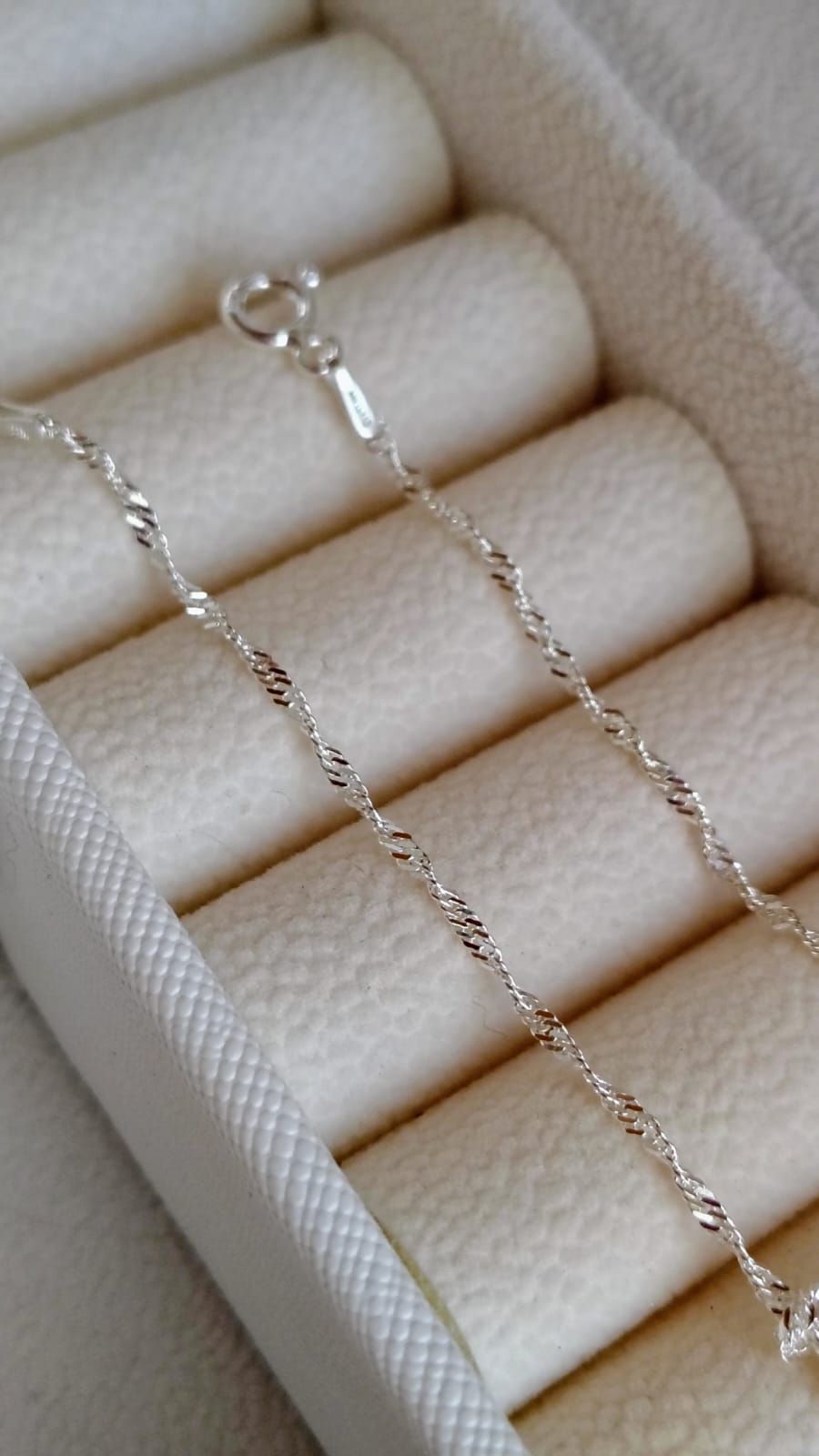 Un delicado collar de cadena de plata cuelga de una mano, con un pequeño broche en el extremo.