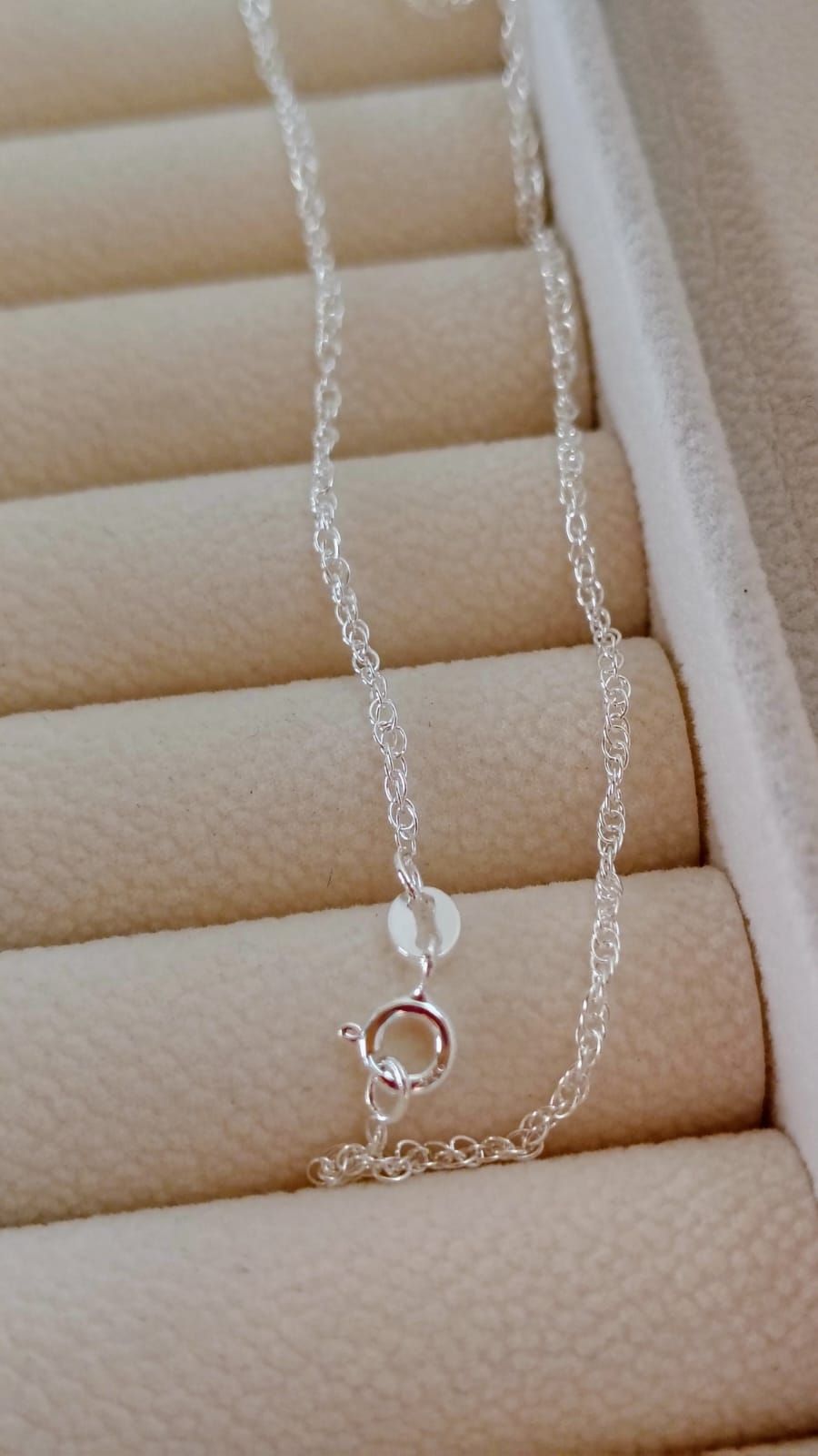 Mano sosteniendo un delicado collar de cadena de plata sobre un fondo de tela blanca suave.