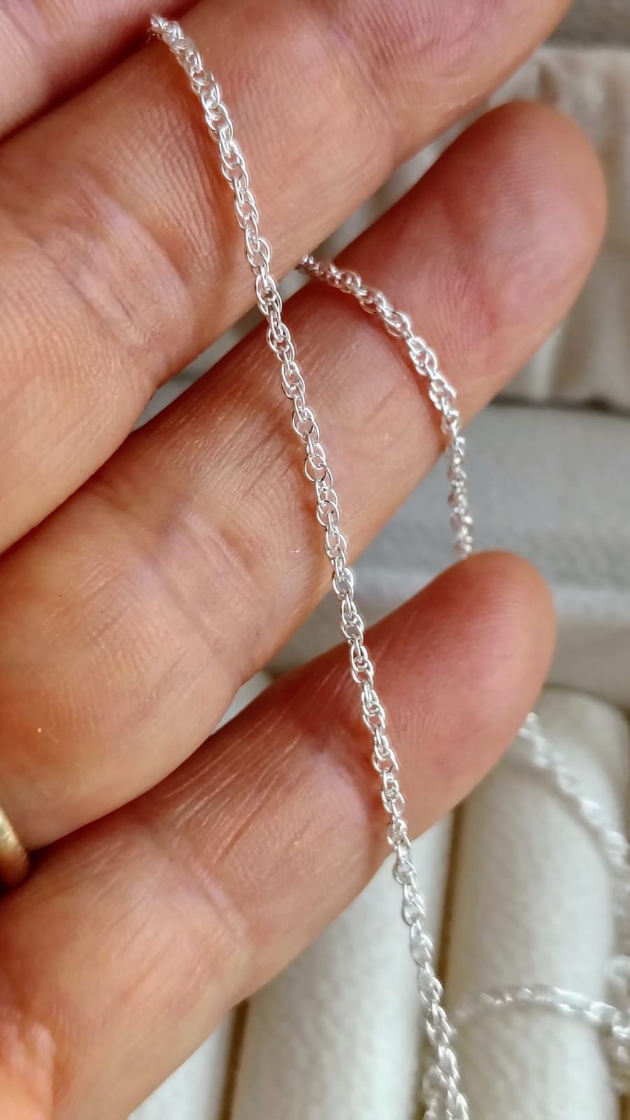 Mano sosteniendo un delicado collar de cadena de plata sobre un fondo de tela blanca suave.