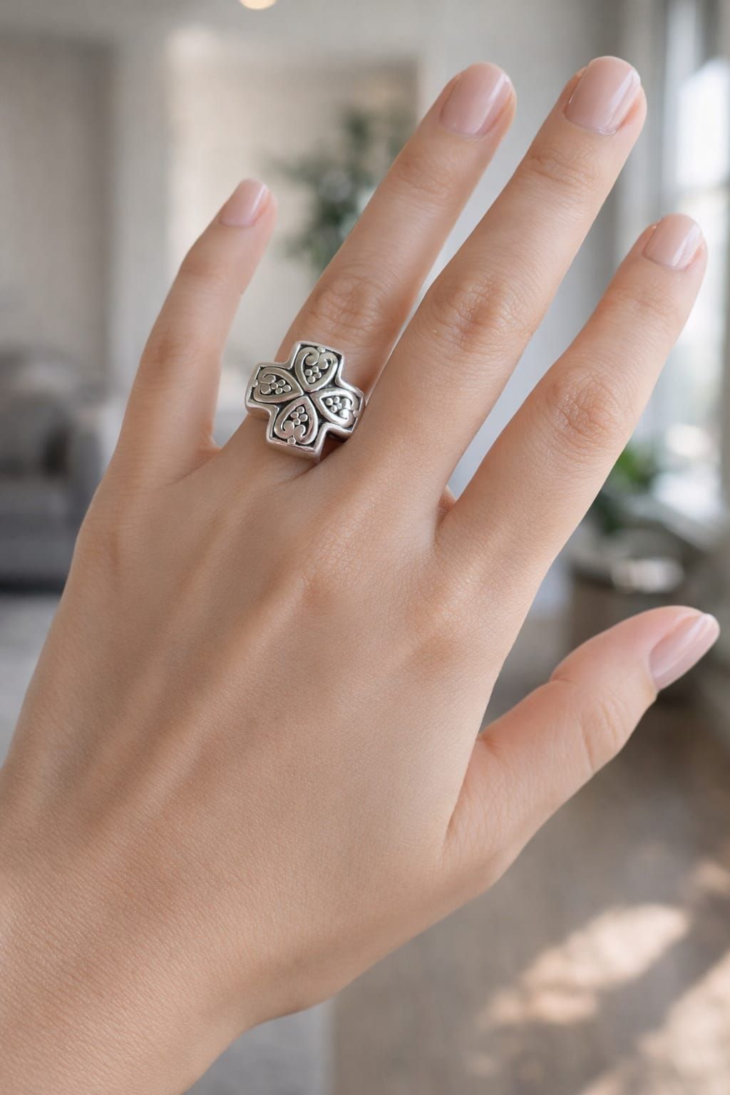 Mano sosteniendo un anillo plateado con forma de trébol con piedras negras y transparentes sobre un fondo suave.